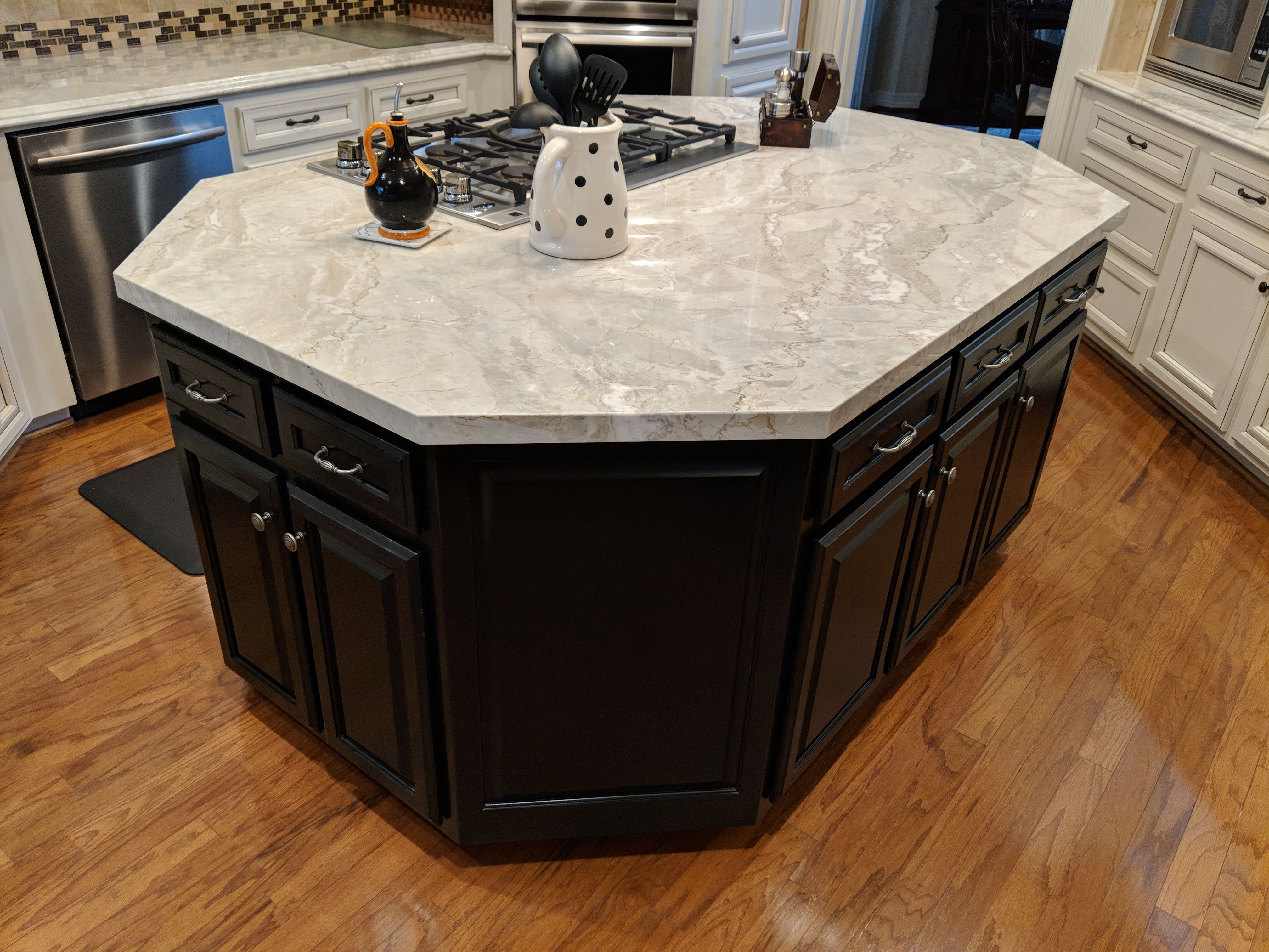 Custom black kitchen island with raised-panel doors, veined stone top, and a built-in gas cooktop