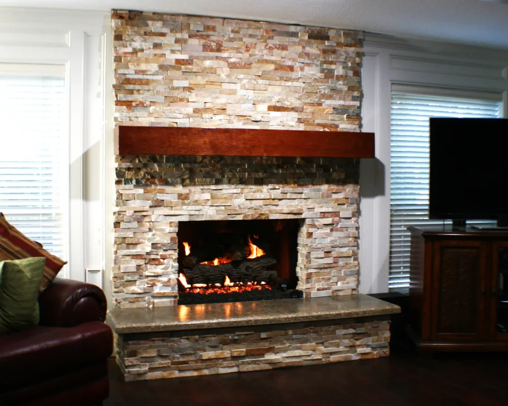 After photo of a Spring TX fireplace remodel: mixed-gray stacked slate, faux-reclaimed cherry mantel, gray-washed concrete hearth, gas logs lit.