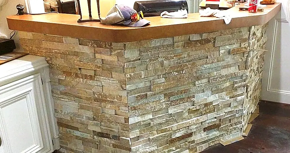 Stacked slate wrapped around the existing bar next to the fireplace so the two pieces read as one wall.