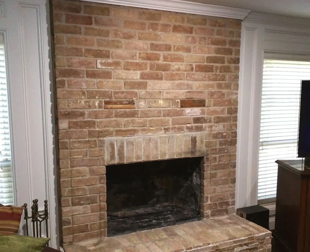 Before photo of the same Spring Texas fireplace — dated tan brick face, empty firebox, and old brick hearth before the slate remodel.