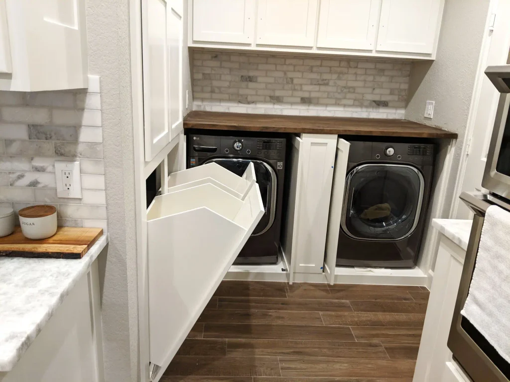 Pull-out hampers in the kitchen laundry run, opening toward the master closet.