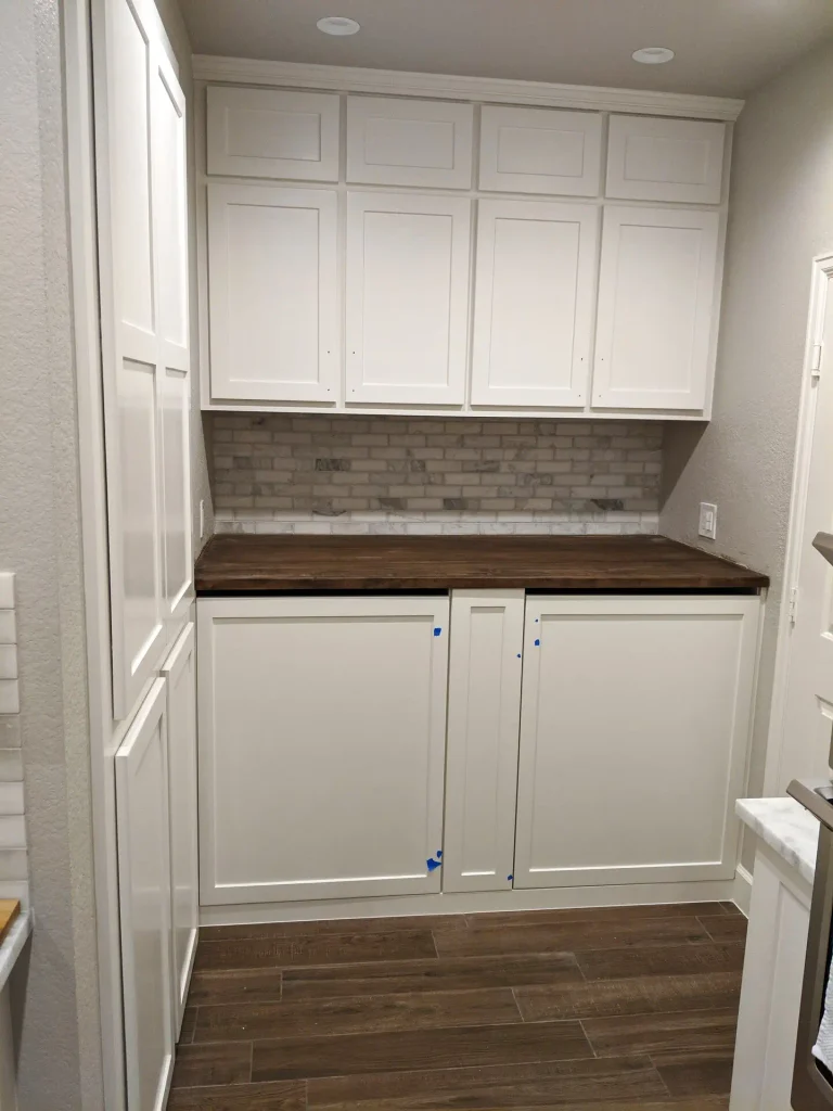 Laundry hidden in a Spring TX kitchen — washer and dryer behind closed cabinet doors and a maple top.