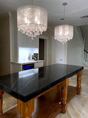 Kitchen island with turned wood legs and a black countertop under crystal chandeliers