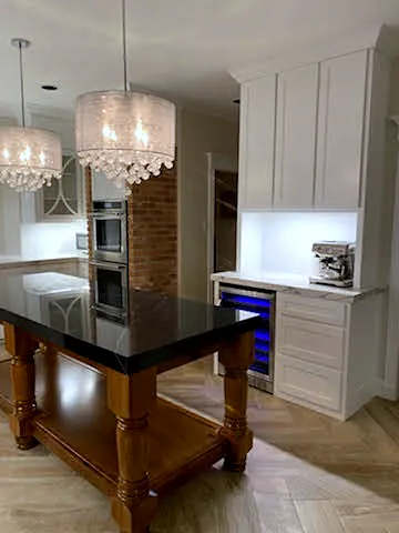 Wood-leg kitchen island with a black top in front of a white cabinet coffee bar